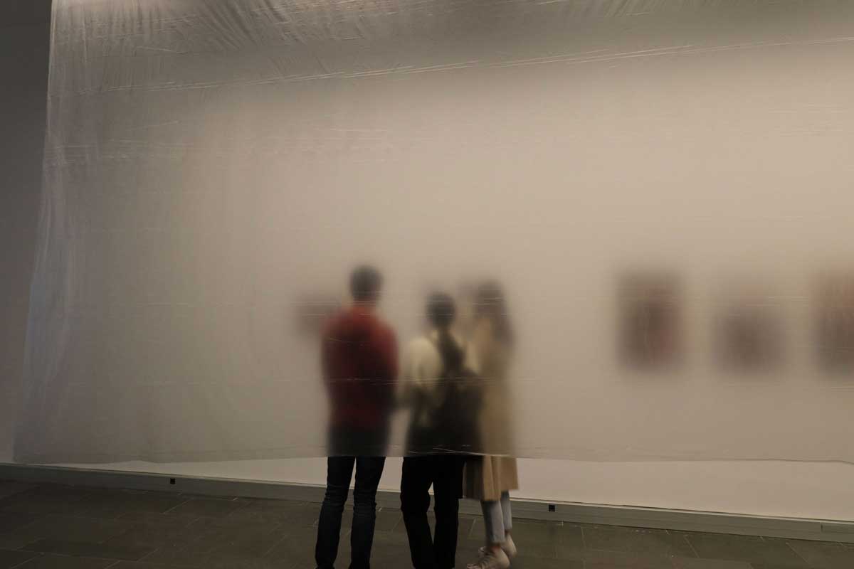 Fotografía de un grupo de personas en la exposición, detrás de una cortina de plástico.