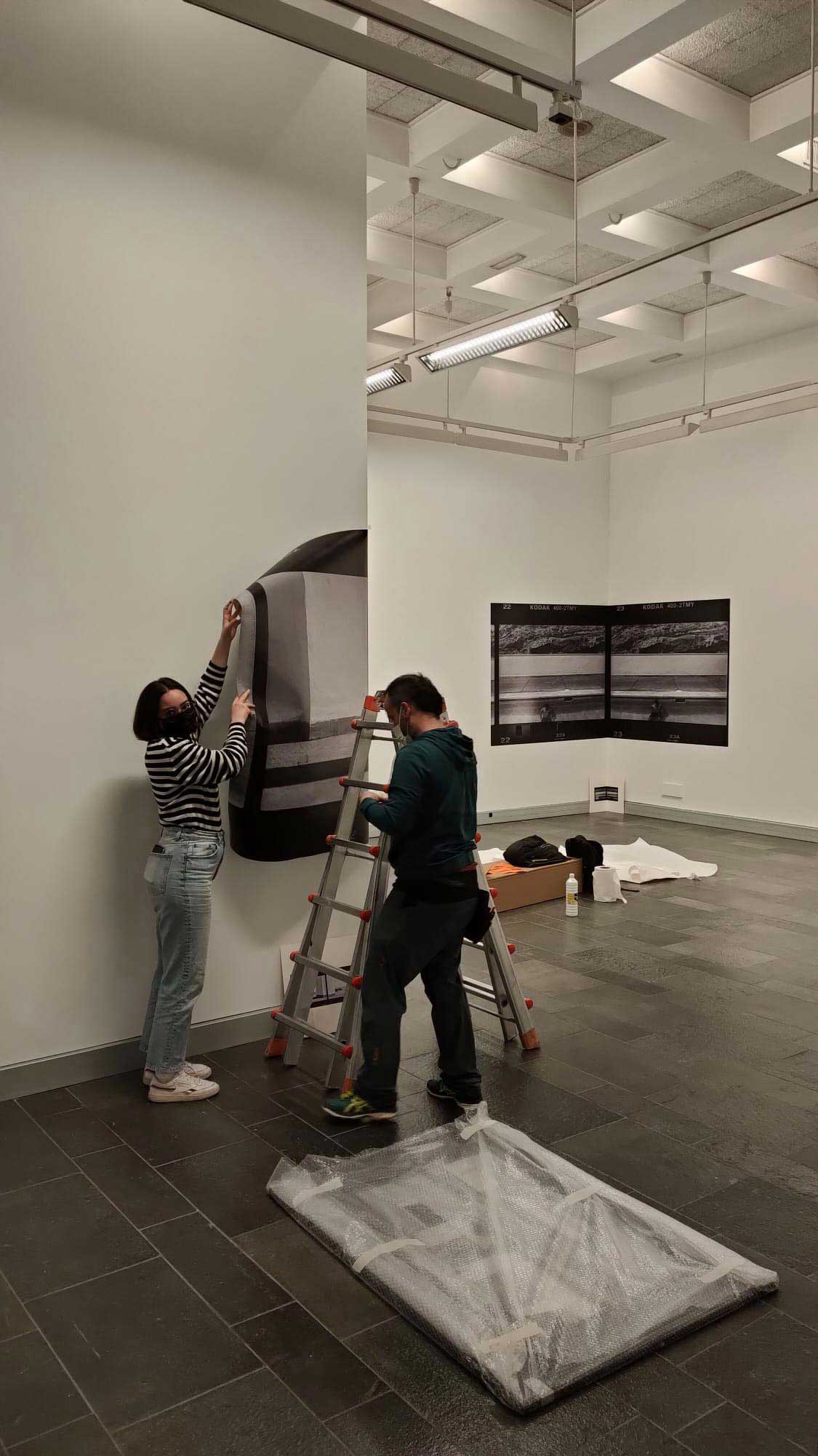 Proceso de montaje de la exposición, donde una compañera de Habemus apoya al montador de gráficas San Martin a pegar una de las fotografías en la pared.