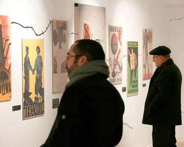 Fotografía de asistentes de la exposición observando unos carteles colgados en la pared.